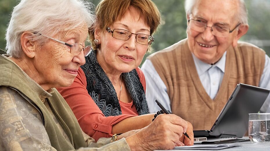Drei Senioren sitzen versammelt um einen Laptop an einem Tisch und besprechen ein Anliegen.